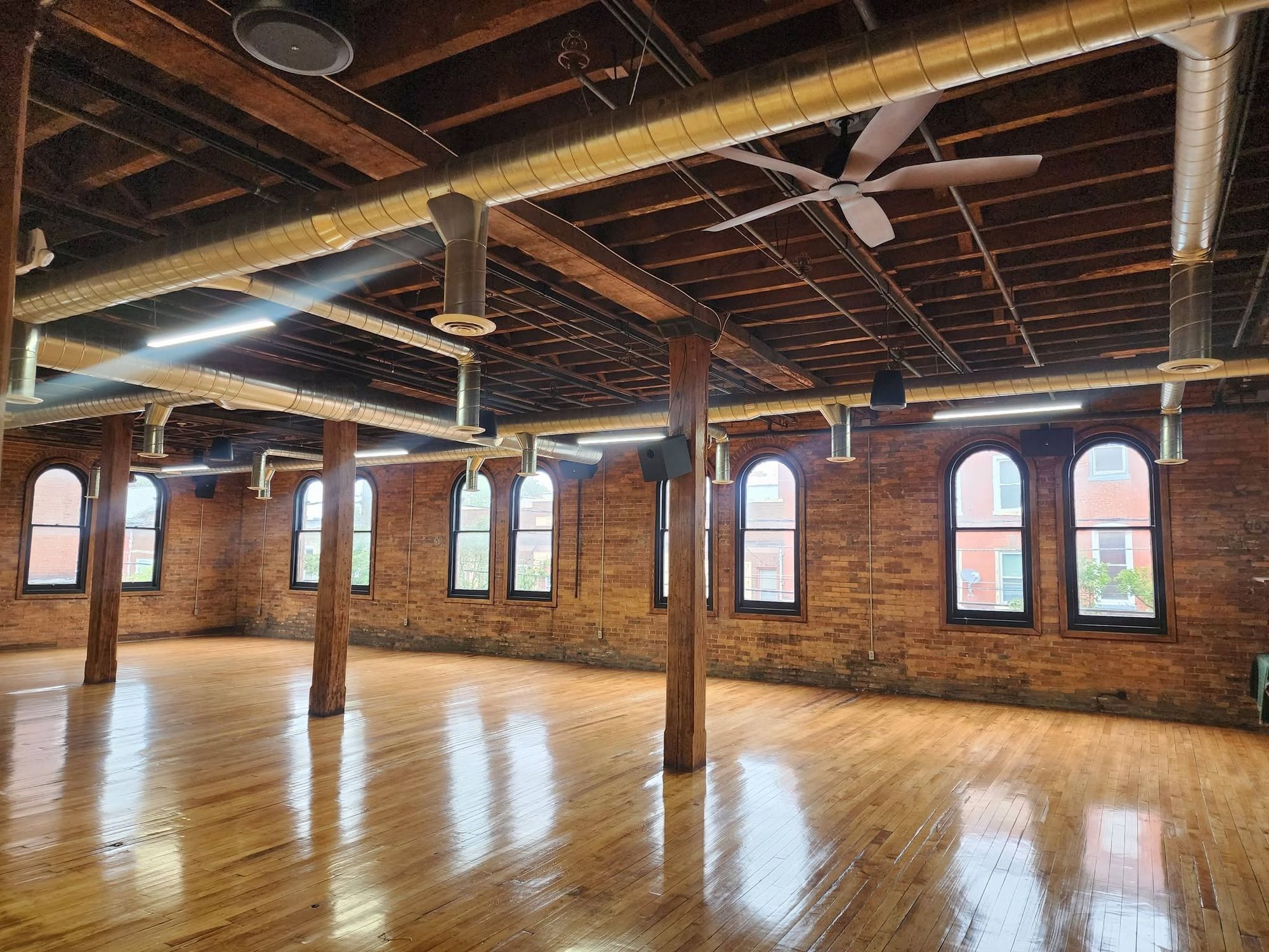 The open hall: hardwood floor, timber posts, and arched windows in exposed brick